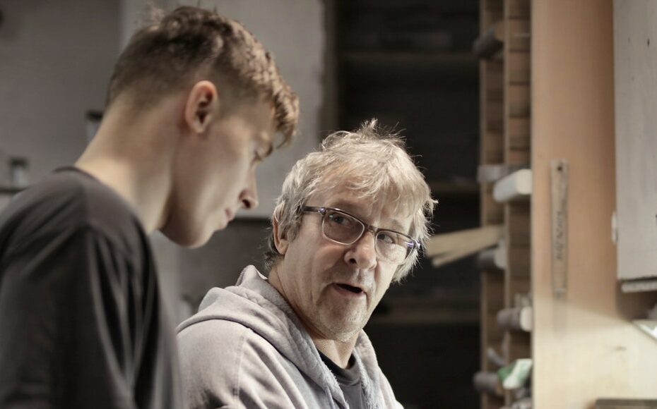 Side view of senior foreman in eyeglasses showing to trainee how handling detail in workshop